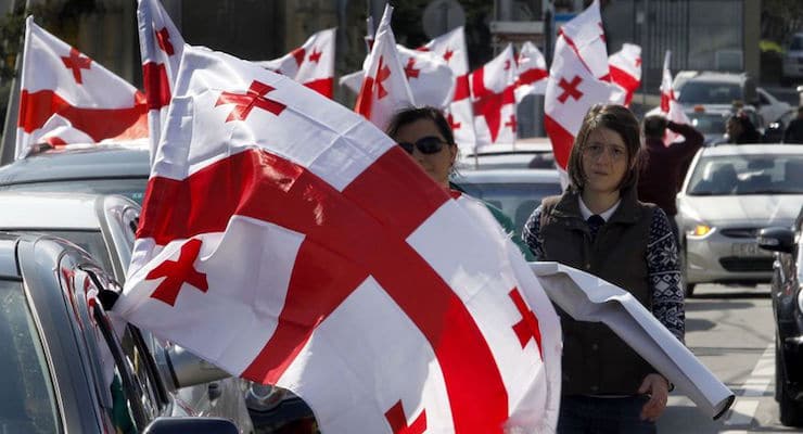 Supporters of the main opposition party wave Georgian national flags during a protest against buying gas from state-controlled Gazprom, in Tbilisi, Georgia, Sunday, March 6, 2016. Thousands of Georgians formed a human chain stretching for about 7 kilometers (4 miles) through the capital on Sunday to protest negotiations between their government and the Russian natural gas monopoly, Gazprom. (AP Photo/Shakh Aivazov)