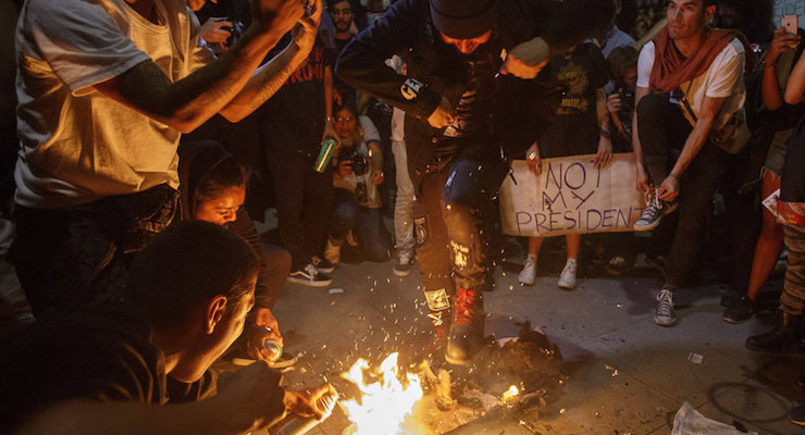 Supporters of Hillary Clinton, along with other groups of fringe radical leftists, burn American flags during protests against the election of President-Elect Donald J. Trump.