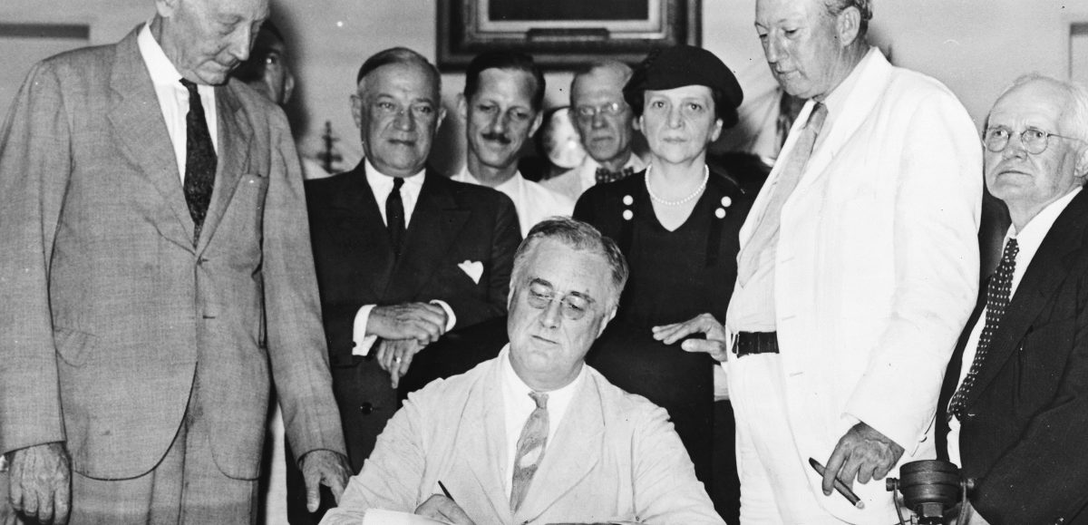President Franklin D. Roosevelt signs the Social Security Act of 1935 on August 14, 1935. Present at the signing was Rep. Robert Doughton (D-NC); unknown person in shadow; Sen. Robert Wagner (D-NY); Rep. John Dingell (D-MI); Rep. Joshua Twing Brooks (D-PA); the Secretary of Labor, Frances Perkins; Sen. Pat Harrison (D-MS); and Rep. David Lewis (D-MD).