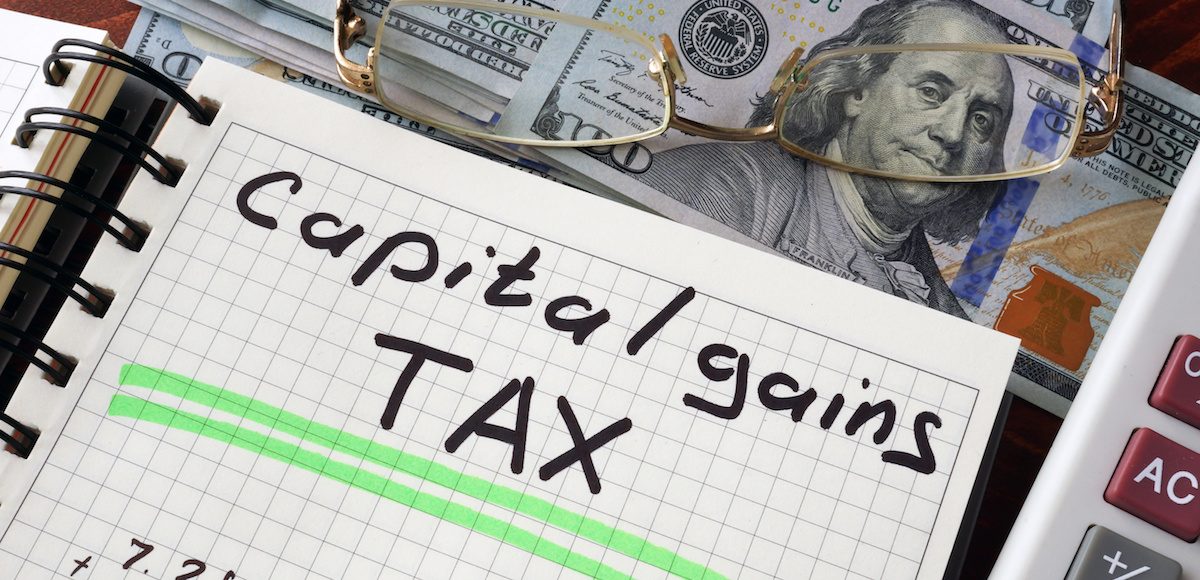 Graphic concept with a notebook and a capital gains tax sign on a table. (Photo: PPD/AdobeStock/Designer491)