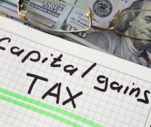 Graphic concept with a notebook and a capital gains tax sign on a table. (Photo: PPD/AdobeStock/Designer491)