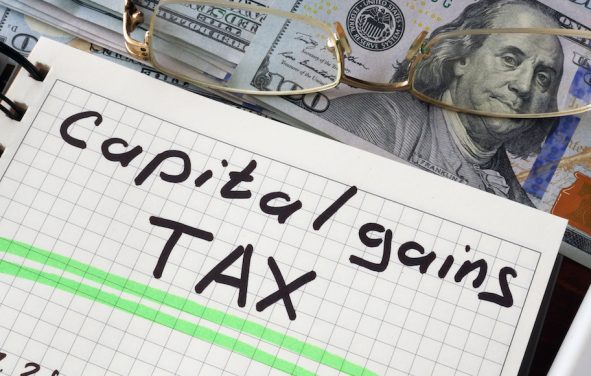 Graphic concept with a notebook and a capital gains tax sign on a table. (Photo: PPD/AdobeStock/Designer491)