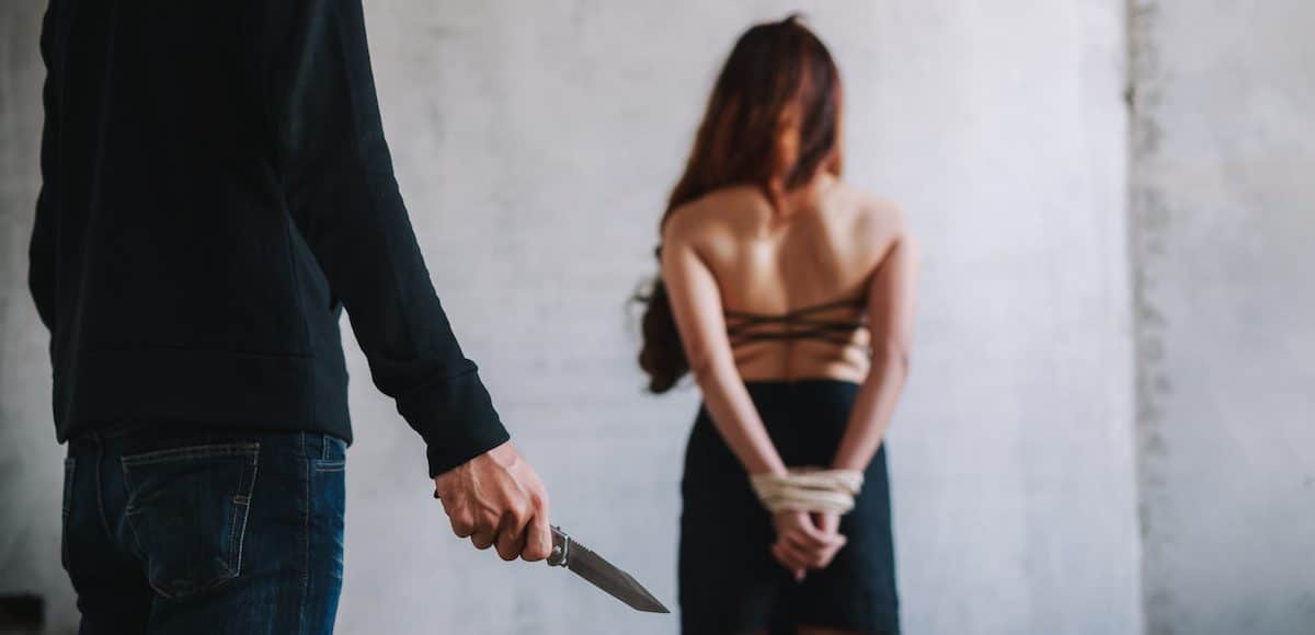 Kidnapping, human and sex trafficking concept of a female hostage and a man holding knife in an abandoned house. (Photo: AdobeStock)