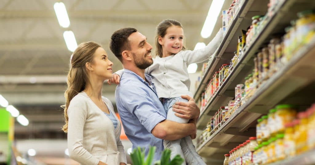 Sale, consumerism and people concept - happy family with child and shopping cart buying food at grocery store or supermarket. (Photo: PPD/AdobeStock/Syda Productions)