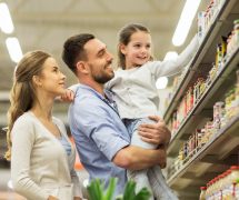 Sale, consumerism and people concept - happy family with child and shopping cart buying food at grocery store or supermarket. (Photo: PPD/AdobeStock/Syda Productions)