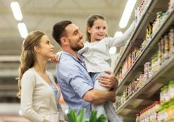 Sale, consumerism and people concept - happy family with child and shopping cart buying food at grocery store or supermarket. (Photo: PPD/AdobeStock/Syda Productions)