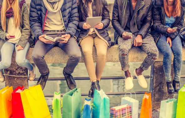 Group of friends sitting outdoors with shopping bags; several people holding smartphones and tablets. (Photo: AdobeStock/ OneInchPunch/PPD)