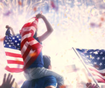 Patriotic holiday. Child sitting on shoulders of her father and holding the Flag of the USA. America celebrate 4th of July.
