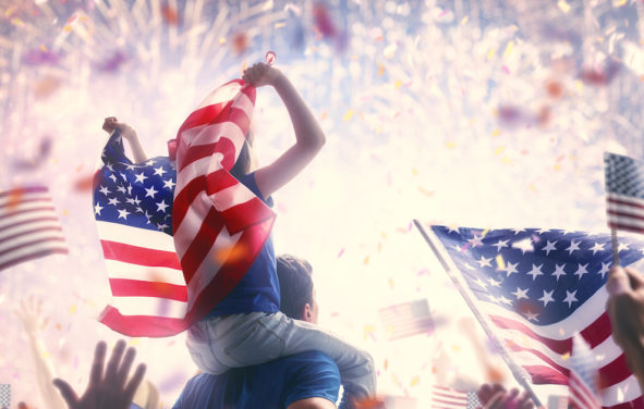 Patriotic holiday. Child sitting on shoulders of her father and holding the Flag of the USA. America celebrate 4th of July.