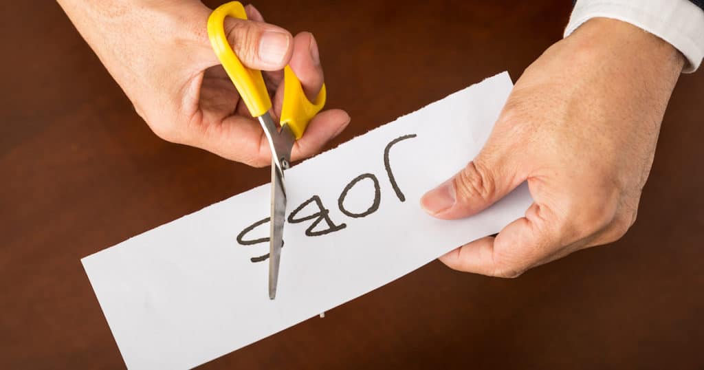 Closeup view of a business man cutting a piece of paper with the word jobs written on it, concept for job cut reports. (Photo: AdobeStock)