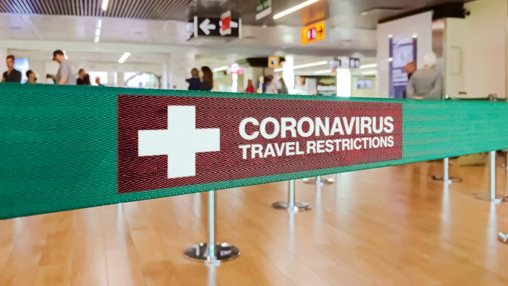 Green ribbon barrier inside an airport with the warning of travel restrictions due to the spread of the Coronavirus, or COVID-19. (Photo: AdobeStock)