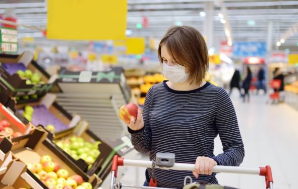 A young woman consumer wearing a disposable medical mask while shopping at the supermarket during the Chinese Coronavirus (COVID-19) outbreak. (Photo: AdobeStock)