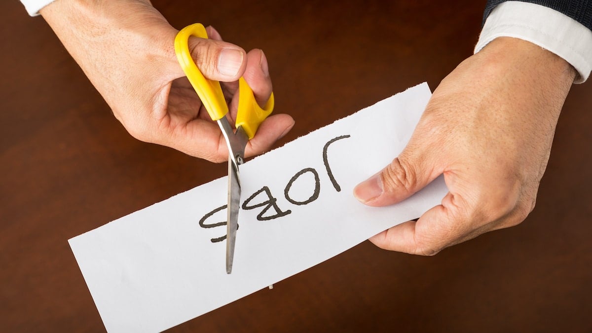 Closeup view of a business man cutting a piece of paper with the word jobs written on it, concept for job cut reports. (Photo: AdobeStock)