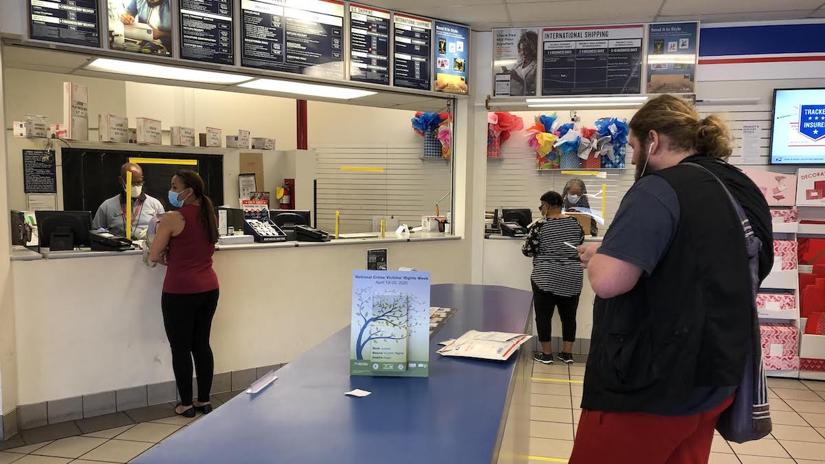 United States Postal Service (USPS) workers don face masks and gloves behind plexiglass at the USPS location on N. Main in Gainesville, Fla., during the coronavirus (COVID-19) pandemic. (Photo: People's Pundit Daily/PPD)