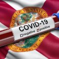 A flag of the state of Florida waving in the wind with a positive coronavirus (COVID-19) blood test tube. (Photo: AdobeStock)