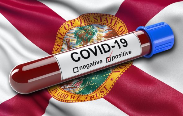 A flag of the state of Florida waving in the wind with a positive coronavirus (COVID-19) blood test tube. (Photo: AdobeStock)
