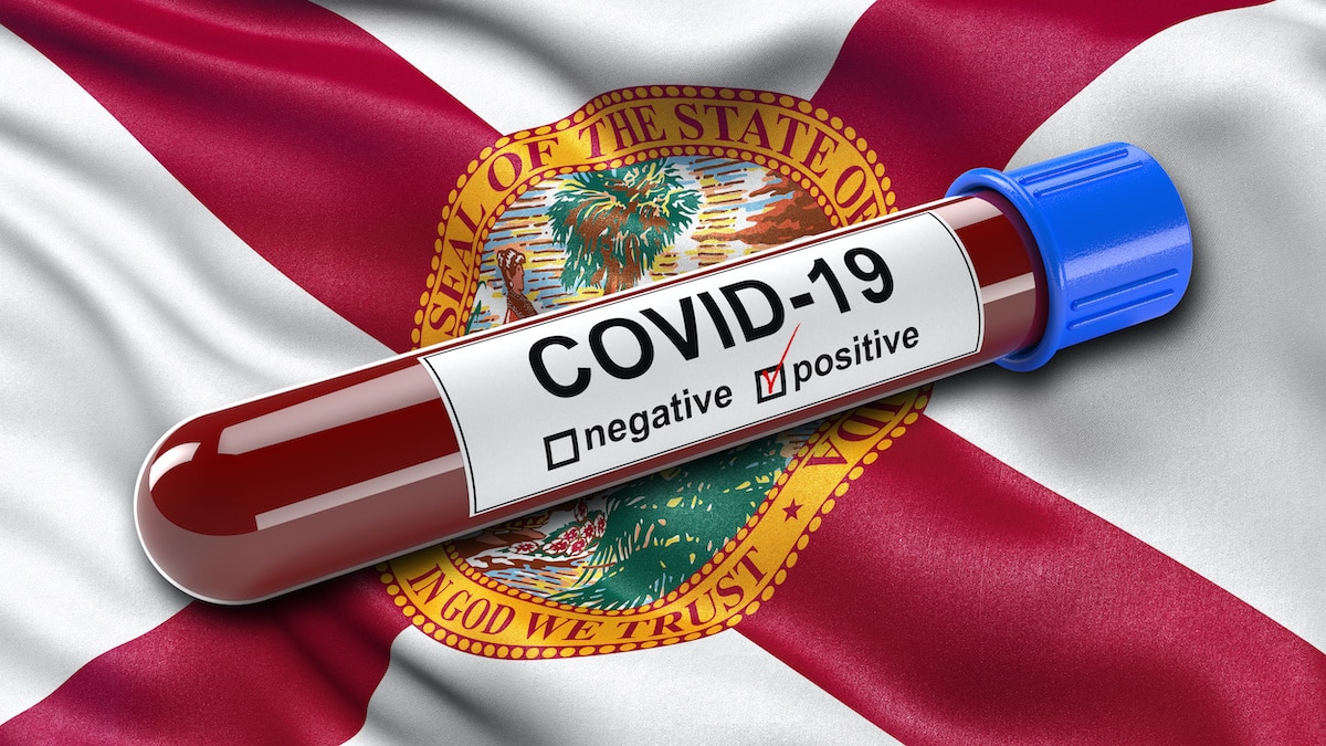 A flag of the state of Florida waving in the wind with a positive coronavirus (COVID-19) blood test tube. (Photo: AdobeStock)