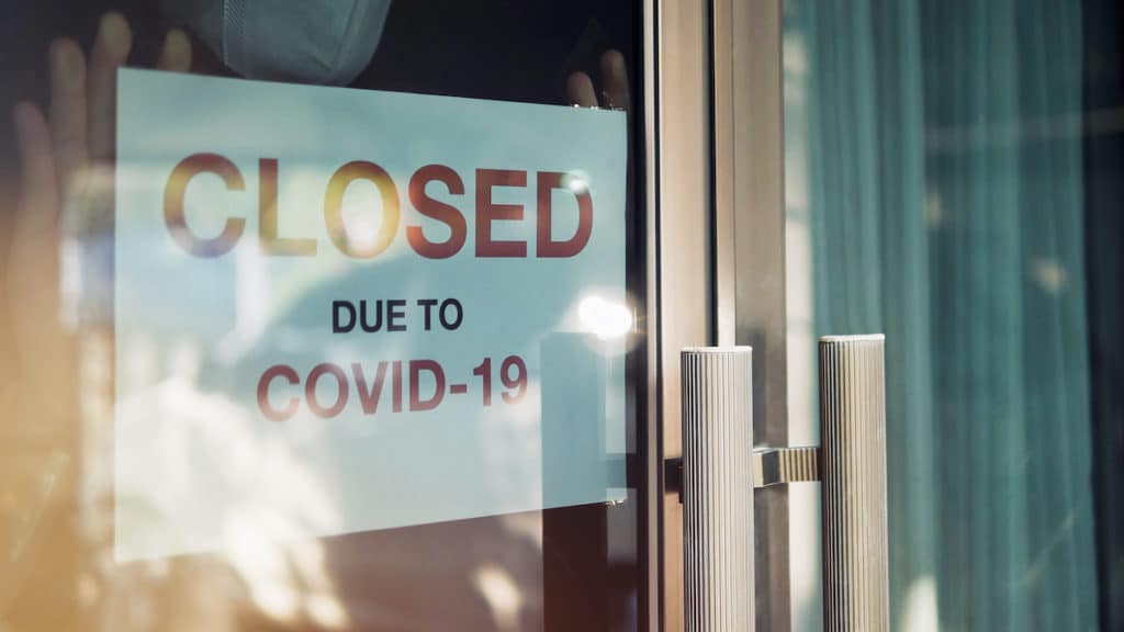 Small business closed business due to the lockdowns to mitigate the spread of Coronavirus (COVID-19). An unidentified person wearing a mask hangs a closed sign on the front door. (Photo: AdobeStock)
