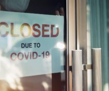 Small business closed business due to the lockdowns to mitigate the spread of Coronavirus (COVID-19). An unidentified person wearing a mask hangs a closed sign on the front door. (Photo: AdobeStock)