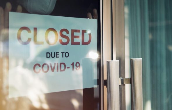 Small business closed business due to the lockdowns to mitigate the spread of Coronavirus (COVID-19). An unidentified person wearing a mask hangs a closed sign on the front door. (Photo: AdobeStock)