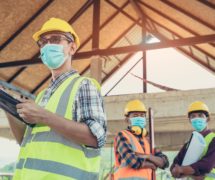 Engineers, construction workers wearing protective masks to prevent dust and infections working together at construction site site amid coronavirus (COVID-19) pandemic. (Photo: AdobeStock)