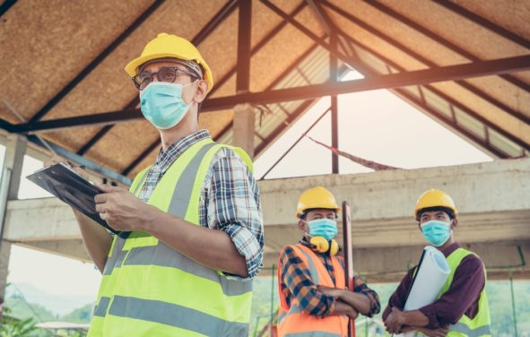 Engineers, construction workers wearing protective masks to prevent dust and infections working together at construction site site amid coronavirus (COVID-19) pandemic. (Photo: AdobeStock)