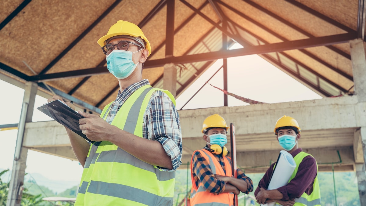 Engineers, construction workers wearing protective masks to prevent dust and infections working together at construction site site amid coronavirus (COVID-19) pandemic. (Photo: AdobeStock)