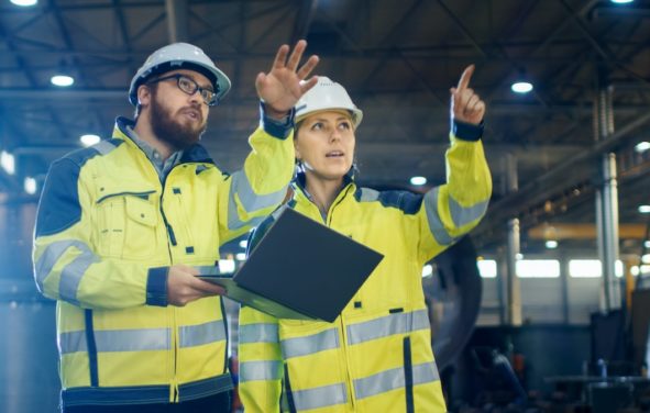 Two engineers — one male and one female — in a manufacturing factory discussing operations in industrial production. (Photo: AdobeStock)