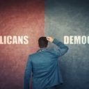 A puzzled businessman and a split wall with Republicans and Democrats written on red and blue sides to illustrate the choice between parties in elections. (Photo: AdobeStock)