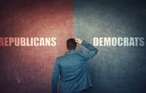 A puzzled businessman and a split wall with Republicans and Democrats written on red and blue sides to illustrate the choice between parties in elections. (Photo: AdobeStock)