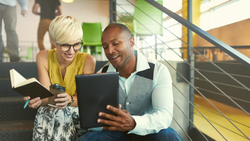 A team of millennial business owners collaborating on an online project using a touchpad tablet in a modern office space. (Photo: AdobeStock/AYAimages)