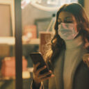 Shop closed due to coronavirus outbreak and woman looking at her mobile device and wearing a surgical mask. (Photo: AdobeStock)