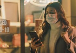 Shop closed due to coronavirus outbreak and woman looking at her mobile device and wearing a surgical mask. (Photo: AdobeStock)